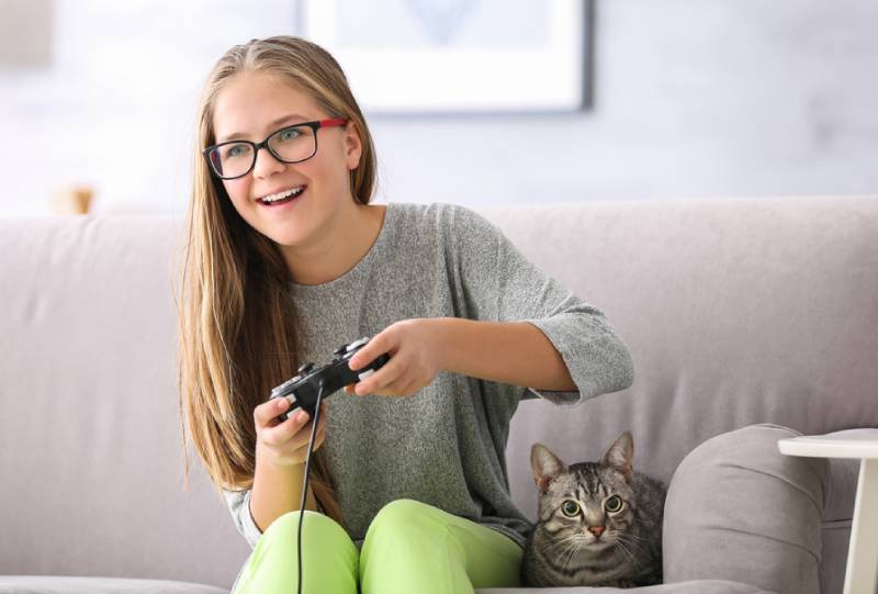 a young girl playing video games with her cat beside her