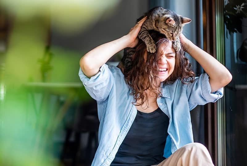 Beautiful-young-woman-laughing-happily-with-a-cat-on-her-head